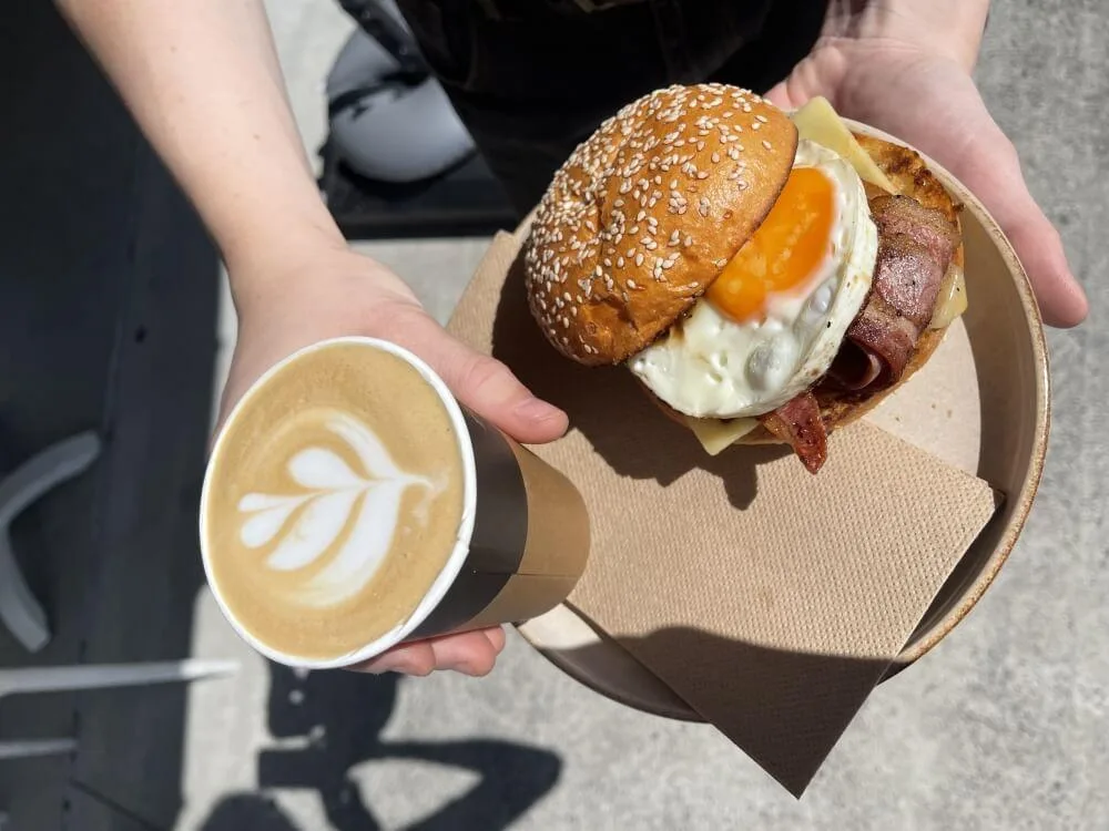 Takeaway coffee and a fresh bacon and egg breakfast roll on a café counter in natural morning light.