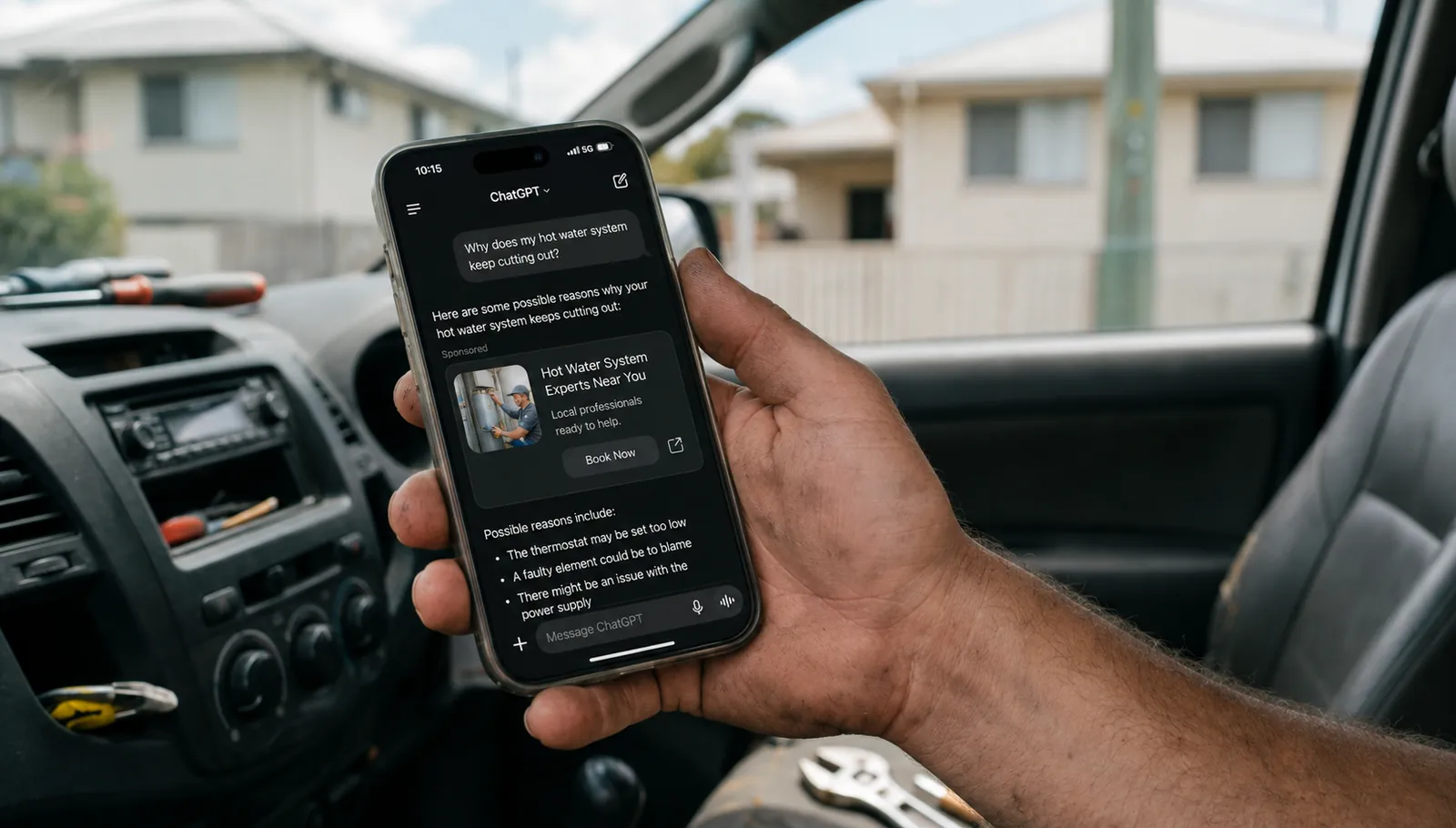 A tradie's hand holding a phone showing a chat interface, ChatGPT Ads Australia, shot from inside a work vehicle